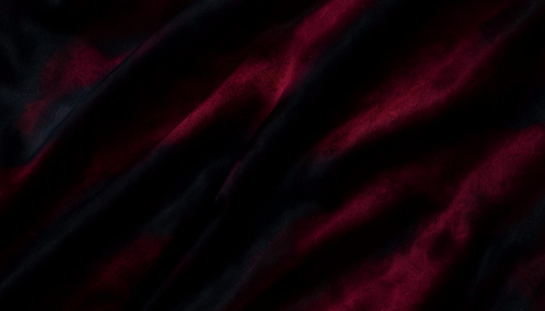 Abstract dark texture resembling folded fabric or a flag, deep crimson and black tones