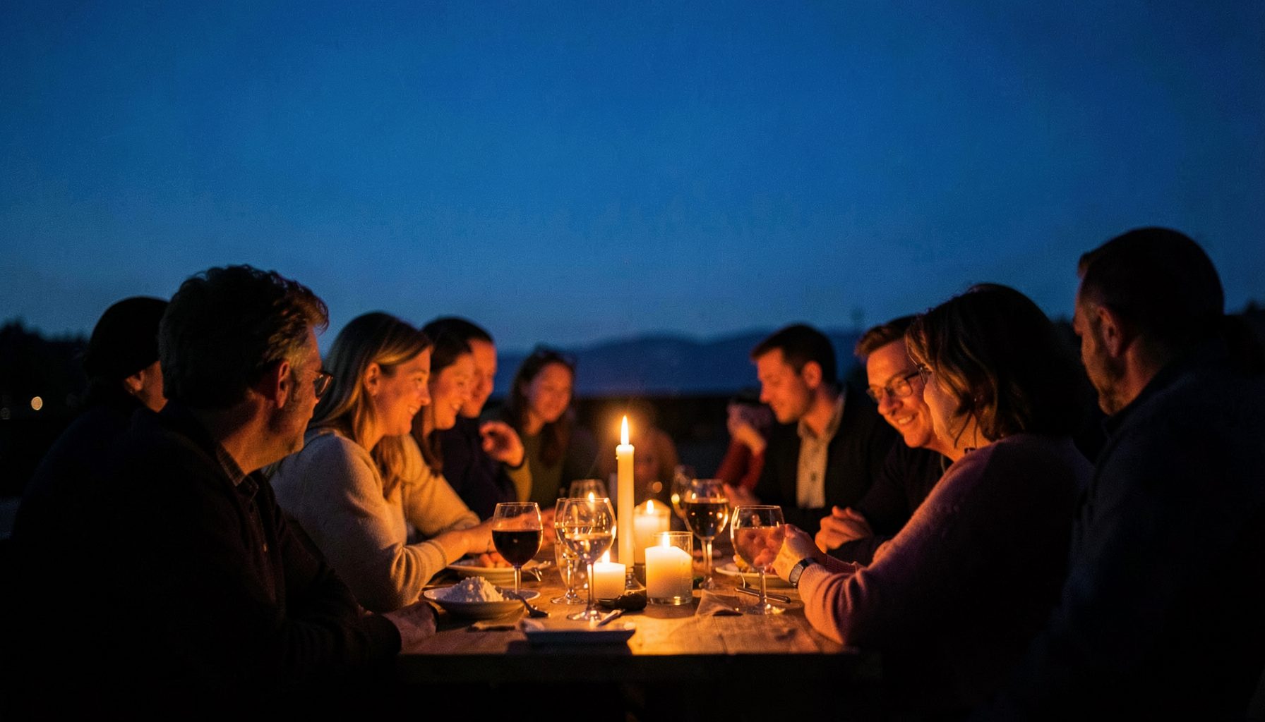 Atmospheric photograph of a candlelit gathering at dusk, warm orange light against deep blue evening sky