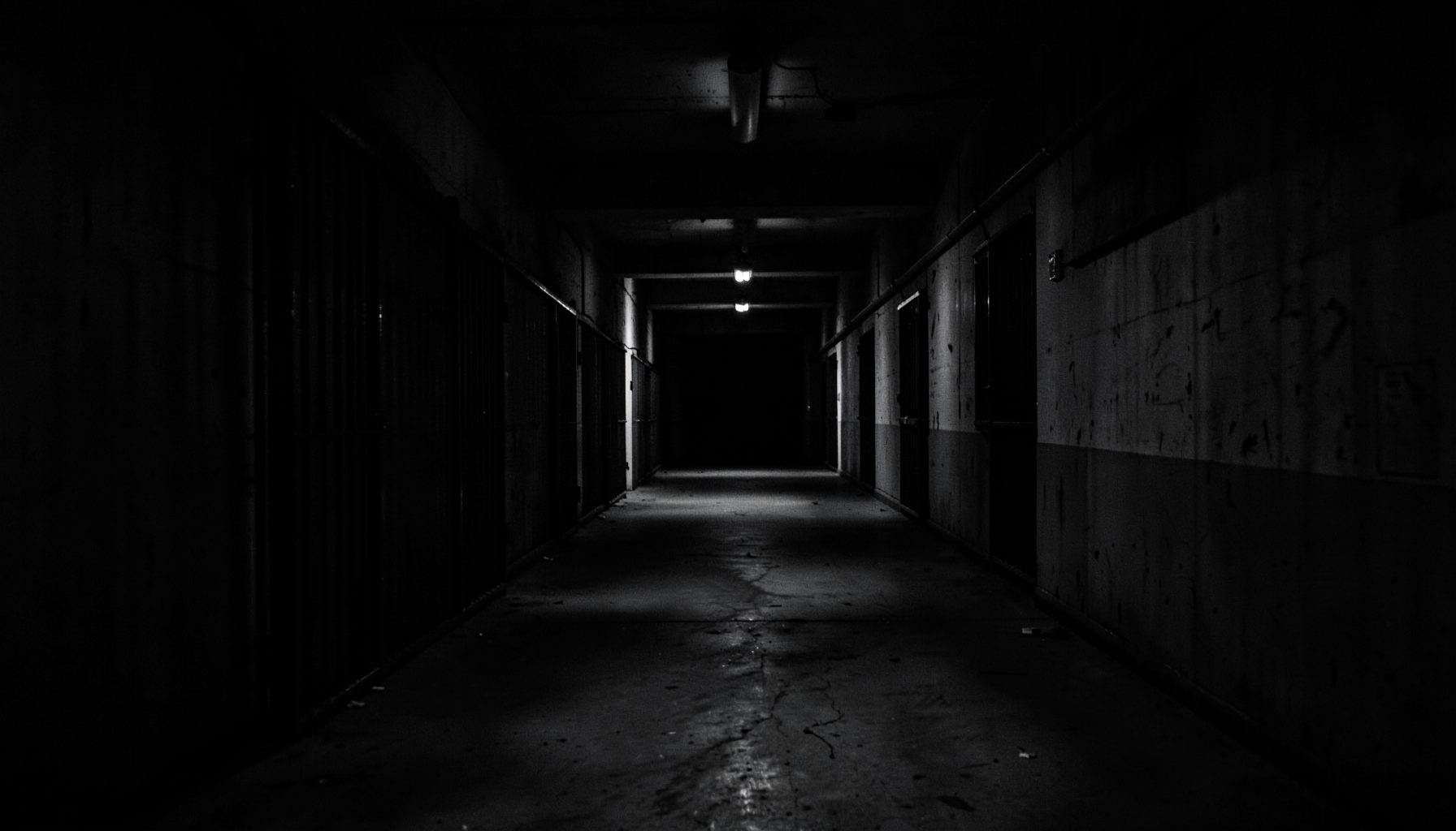 Dark, moody monochrome image of a prison corridor stretching into shadow, evoking solemnity and endurance