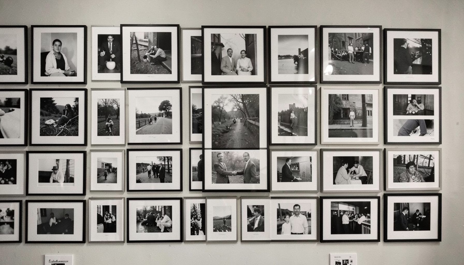 Gallery wall of black and white photographs arranged in a grid, muted tones and documentary style