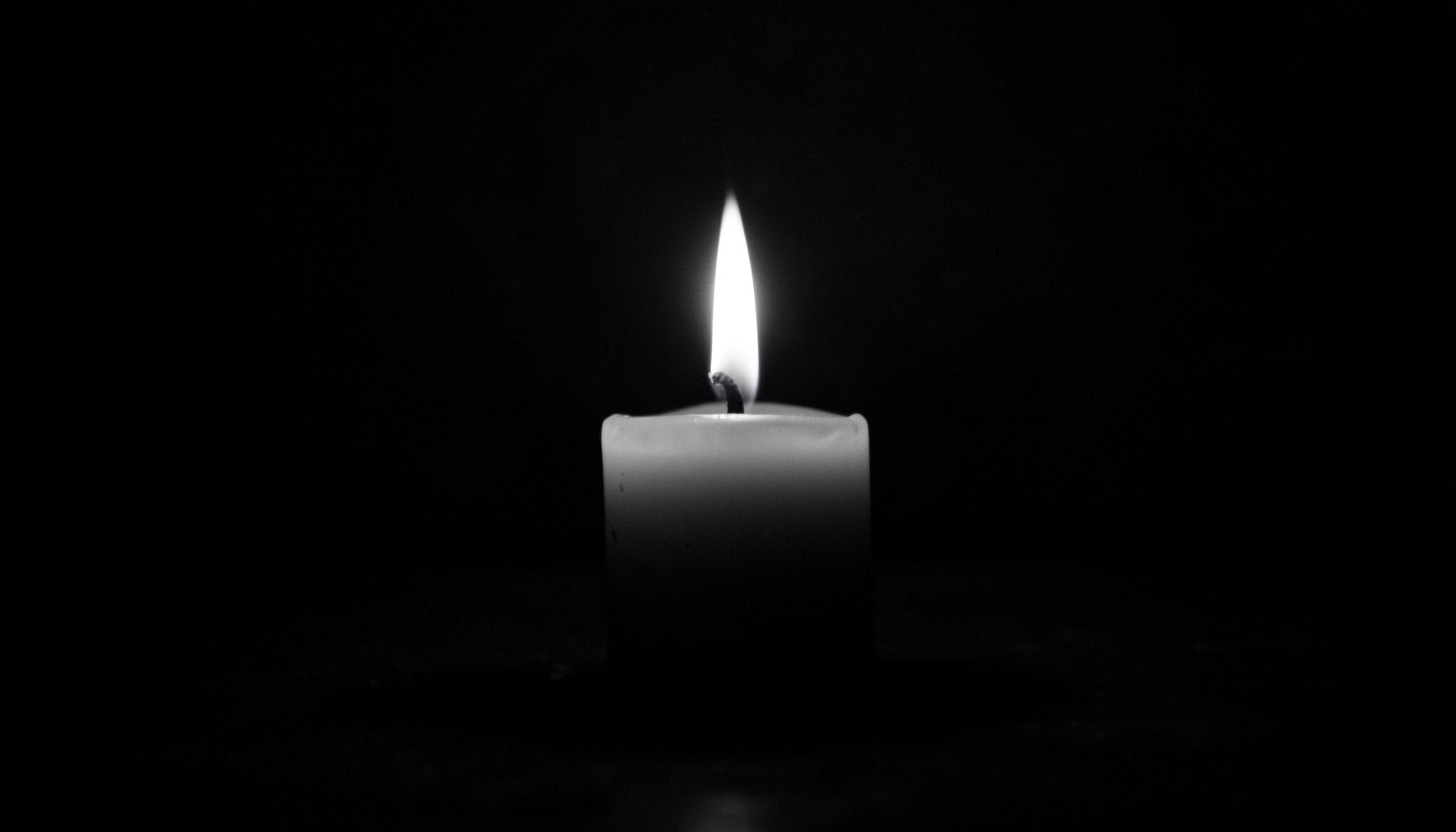 Muted black and white photograph of a single candle burning in darkness, quiet and reflective