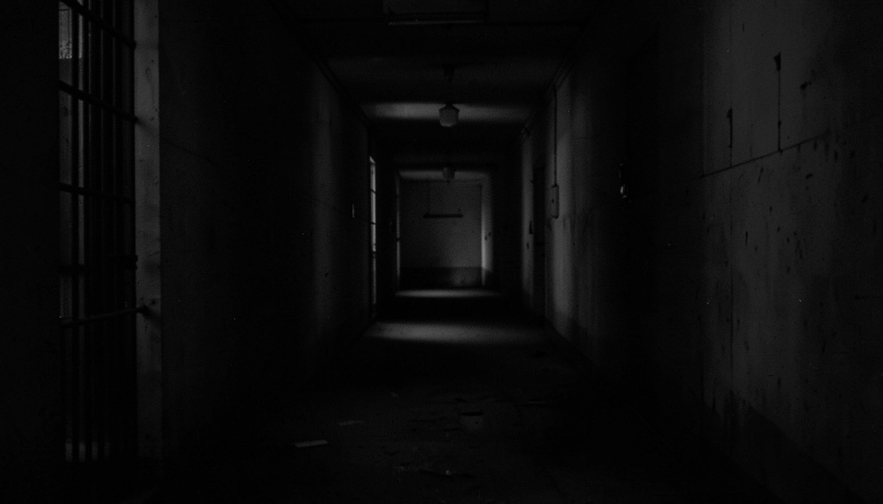 Sombre monochrome image of a prison corridor fading into shadow, evoking isolation and endurance